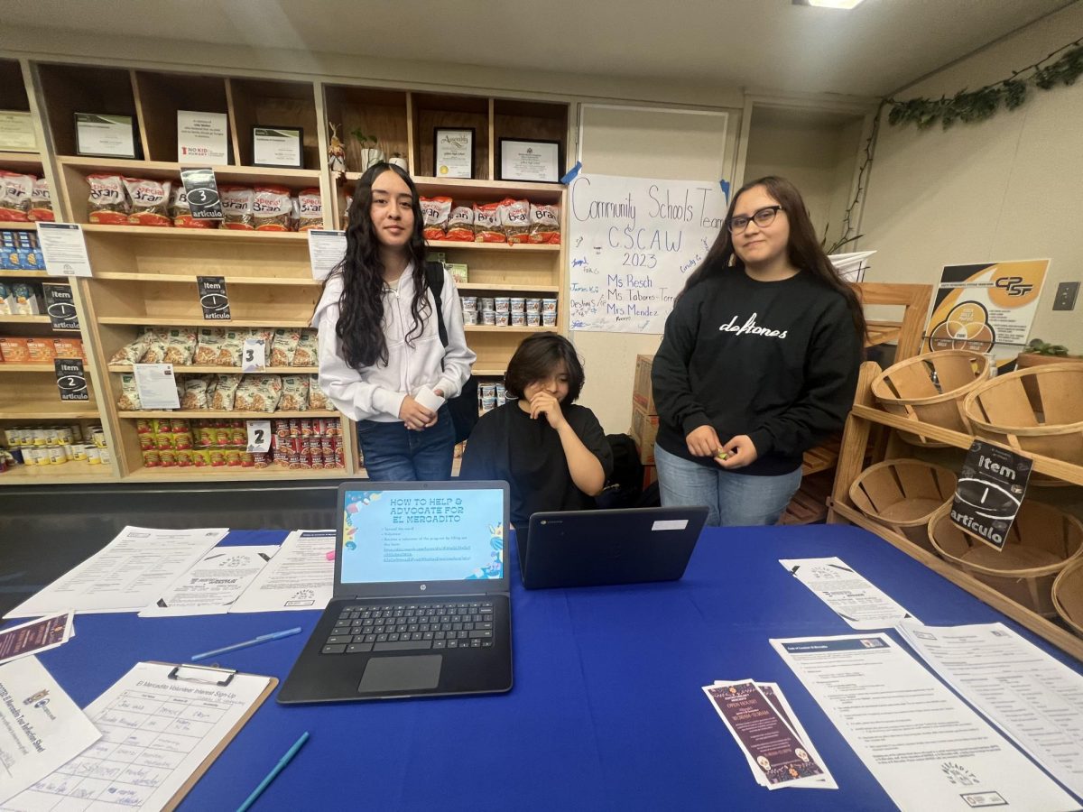 Three student leaders present at the El Mercardito history station where students had the opportunity to sign up to volunteer. 